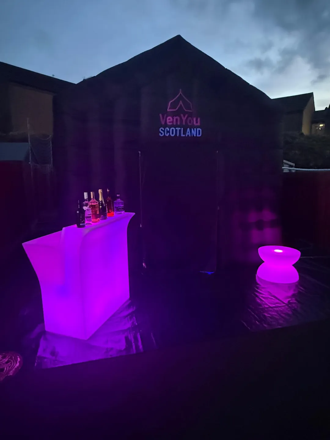 Glowing pink LED bar and stool beside a VenYou tent at dusk